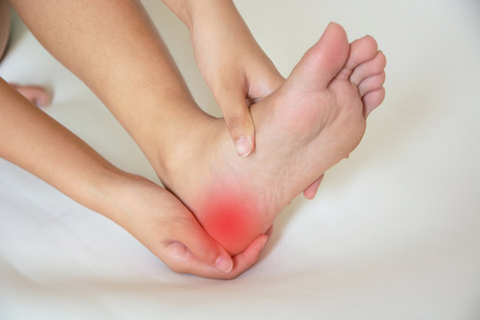 Individual seated on a bed, grimacing while clutching their foot, indicating discomfort or pain